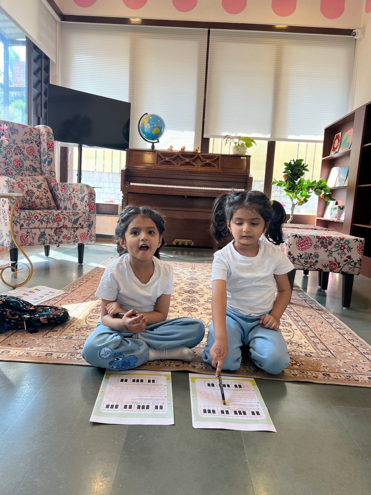 Two girls doing piano note-reading worksheets in front of an upright piano