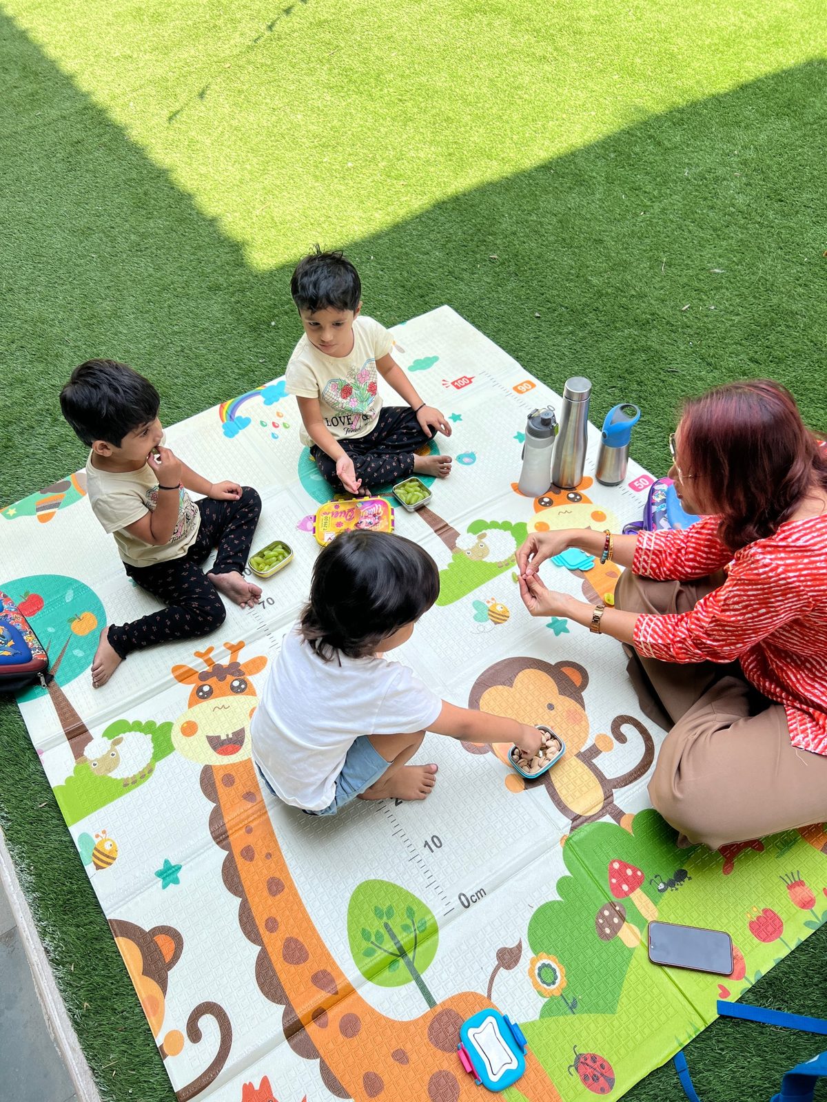 Children sharing snacks on a play mat on the lawn