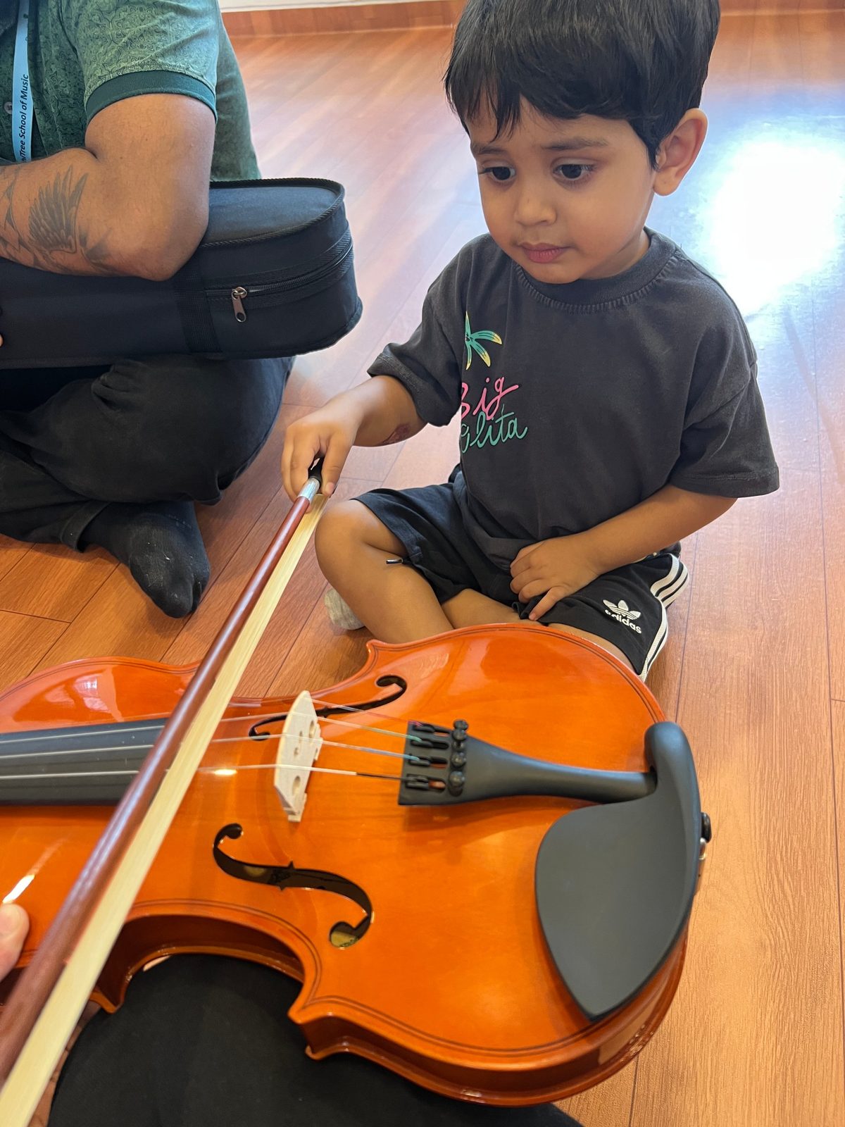 A toddler trying a violin bow with a music teacher